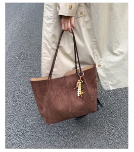 Close-up view of a brown suede tote bag with beaded pendant and slim shoulder straps.