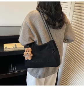 Detailed view of a casual black suede shoulder tote bag with a cute fluffy bear pendant accessory.