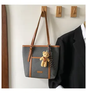 Stylish grey tote bag with brown leather handles, plush bear charm and chic casual design.