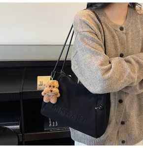 Casual black canvas tote bag detail view with cute bear pendant and letter embossed design.
