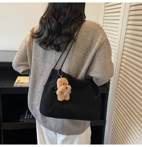 Detail view of woman carrying casual black suede shoulder tote bag with cute teddy bear pendant.