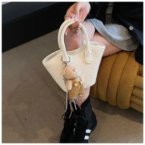 Woven bucket handbag for women, stylish summer shoulder bag with cute bear pendant detail.