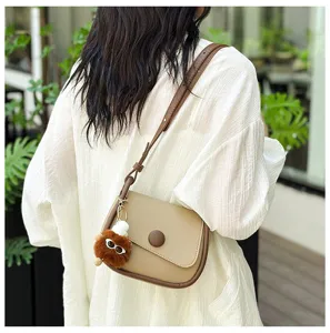 Detailed shot of a stylish khaki crossbody small square bag with a cute fluffy plush charm pendant.