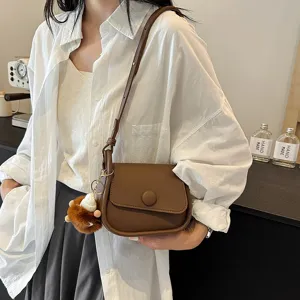 Stylish brown crossbody bag for women, chic small saddle bag with cute plush pendant.