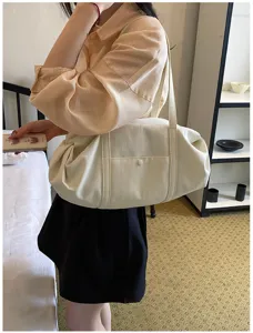 Detail view of a soft creamy white shoulder tote bag worn by a model in an indoor lifestyle scene.