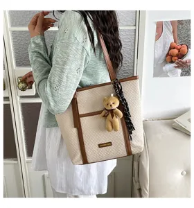 Stylish canvas tote bag with brown trim, cute bear pendant, and scarf detail for daily use.