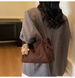 Detail shot of casual brown suede shoulder bag featuring cute plush bear charm for daily use.