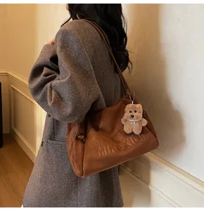 Brown suede shoulder tote bag featuring a cute plush bear pendant, casual daily style detail.