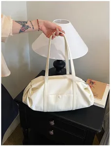 Detailed view of the casual white shoulder bag with pleated design and top handles on table.