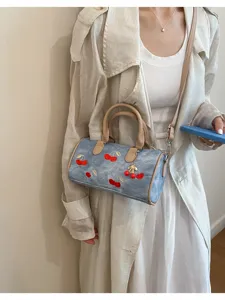 Chic denim barrel shoulder bag featuring charming embroidered cherries and a cute pendant detail.