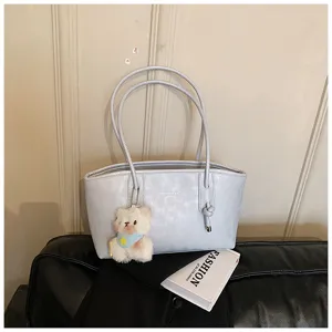 Light blue leather tote bag detail, featuring dual handles, knot accent and cute bear pendant.