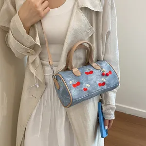 Chic denim blue boston shoulder bag with cute red cherry embroidery and matching tan handles.