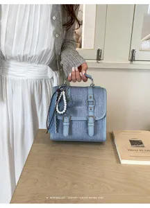Sac à dos bandoulière rétro en denim bleu avec boucles doubles et pendentif perle.