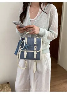 Mini sac à dos rétro en denim avec bordure en cuir blanc, pendentif perle et poignée pour femme.