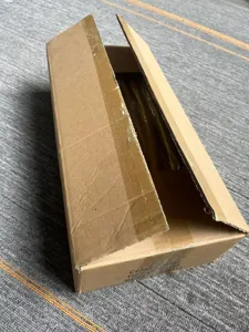 Détail de l'emballage du support d'arche en métal montrant les tubes du cadre doré dans la boîte.