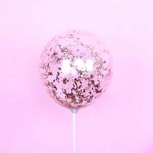 Close-up of clear bubble balloon filled with rose gold confetti sequins on white stick.