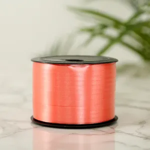 Close-up detail of coral pink ribbon roll for gift wrapping and balloon decoration use.