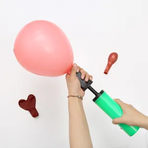 Detail view of a portable plastic manual hand balloon air pump in action inflating a pink balloon.