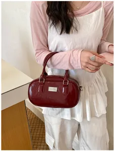 Detailed view of burgundy patent leather bowling handbag with metal plate and handles.
