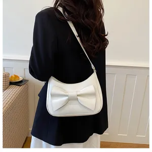 Detail shot of white shoulder bag with elegant bow accent, showing texture and design features.