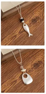 Close-up detail view of elegant silver long pendant necklace with unique metal fish charms.
