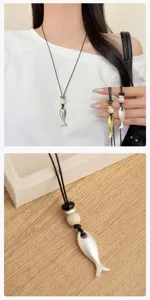 Dettaglio collana maglione con ciondolo a pesce in corda di pelle nera, gioielli minimalisti.