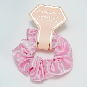 Détail d'un chouchou en satin rose avec une carte de demoiselle d'honneur dorée