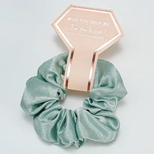 Gros plan d'un chouchou en satin vert menthe avec une étiquette cadeau de demoiselle d'honneur.