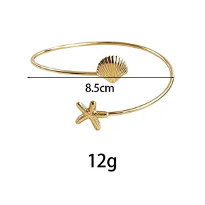 Detalle de brazalete abierto de metal dorado con delicado diseño de concha y estrella.