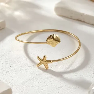 Hermoso detalle de pulsera abierta dorada con concha y estrella de mar estilo playa.