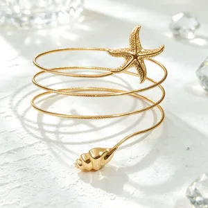 Primer plano del brazalete de brazo en espiral dorado con diseño de estrella de mar y concha.