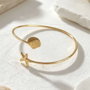 Brazalete abierto dorado con dijes de concha y estrella de mar estilo playa de verano.