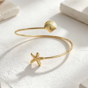 Brazalete abierto dorado con dijes de concha y estrella de mar para la playa de verano.