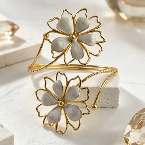Detailed view of gold-tone open cuff bracelet featuring dual white enamel flower charms.
