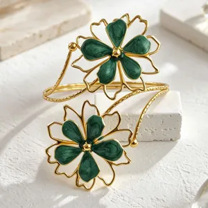 Gold tone open cuff armlet featuring dual green enamel flower designs for trendy fashion.