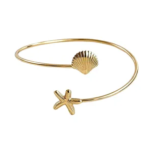 Brazalete abierto de metal dorado con dijes de concha y estrella de mar para verano.