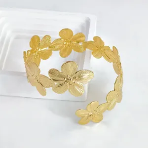 Vista detallada del elegante brazalete rígido de metal dorado con flores delicadas.