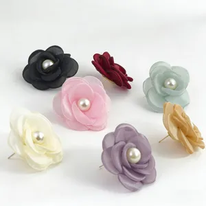 Vista detallada de pendientes de botón con perla y flor de camelia de tela colorida.