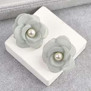Detalle de pendientes de tachuela con perla y flor de camelia de tela gris, moda dulce.