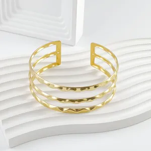 Detalle del brazalete abierto ondulado dorado con diseño texturizado de triple capa.