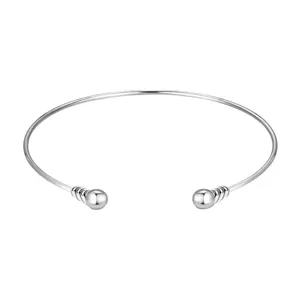Primer plano detalle de pulsera brazalete abierta plateada con extremos esféricos.