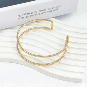 Bracciale manchette aperto multistrato in metallo dorato, design geometrico chic, gioiello minimalista.