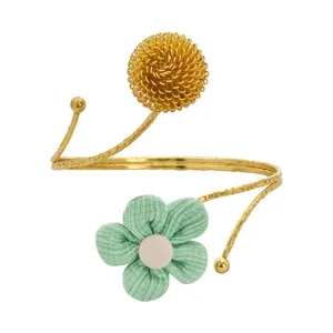 Goldener offener Armreif mit strukturierter Metallkugel und grüner Stoffblume als Dekoration.