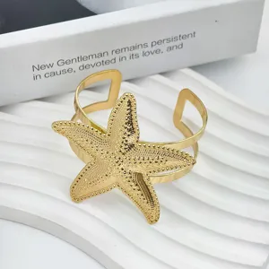 Gouden zeester open manchet armband, chique metalen zomer strand polssieraad detail.