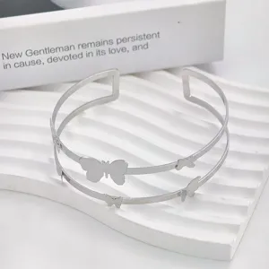 Dettaglio ravvicinato di bracciale manopola in metallo doppio con charm a farfalla.