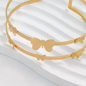 Primo piano dettagliato di un bracciale rigido aperto in metallo dorato con farfalle traforate.