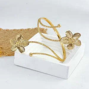 Vista detallada del brazalete abierto dorado con extremos florales delicados y diseño texturizado.