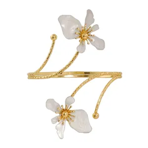 Brazalete de brazo abierto dorado con dijes de flores blancas, accesorio de moda ajustable.