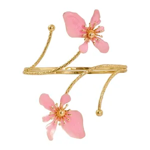 Brazalete abierto dorado con encantadores detalles florales rosas y finas ramas delicadas.