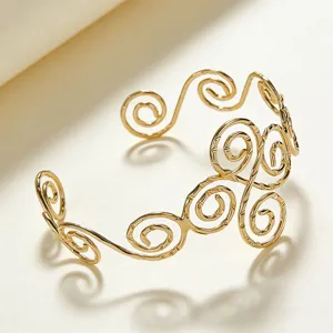 Dettaglio del bracciale da braccio aperto a spirale in metallo dorato, stile retrò.